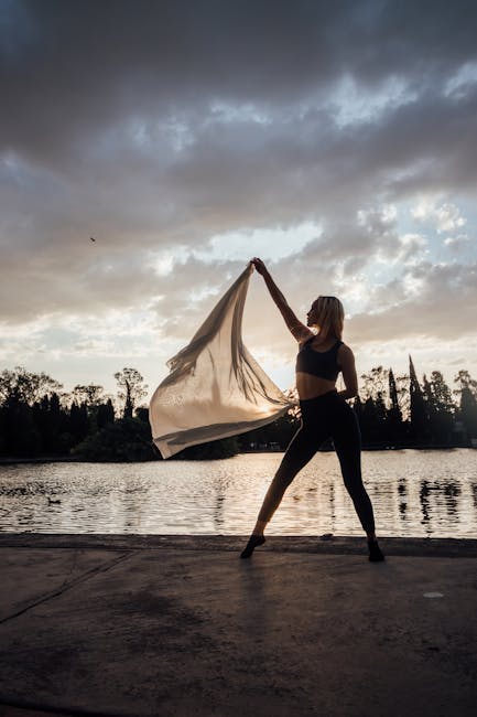 Woman practicing yoga outdoors in a graceful pose near the water.